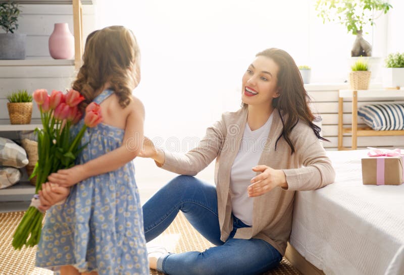 Happy mother`s day! Child daughter is congratulating mom and giving her flowers tulips. Mum and girl smiling. Family holiday and togetherness