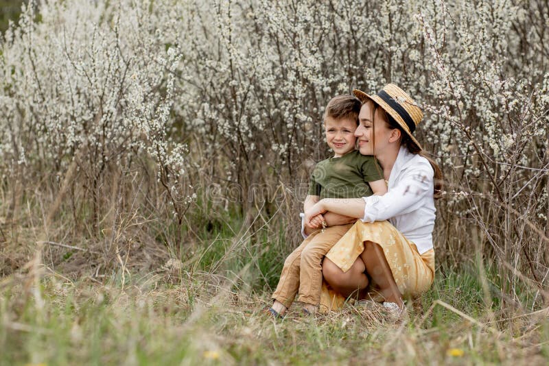 Happy mother and son having fun together. Mother gently hugs her son. In the background white flowers bloom. Mother`s day