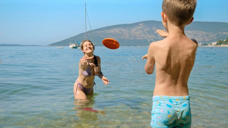 Happy mother with son playing frisbee on the sea beach. Family holiday, vacation and fun summertime of children and