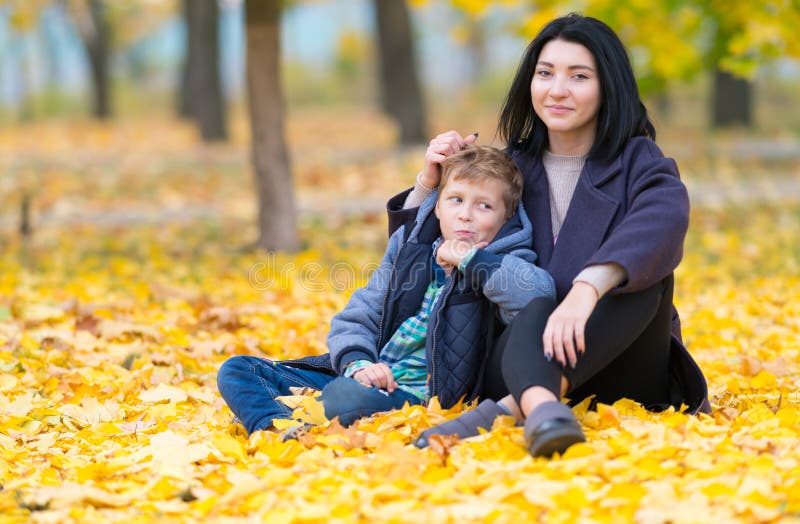 Happy mother and son sitting in yellow fall leaves.