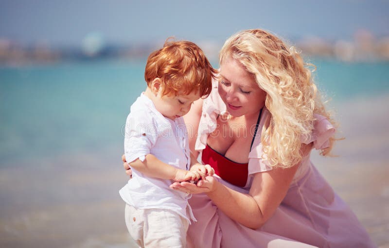 Happy mother with baby son playing with pebble stones on the beach, summer vacation