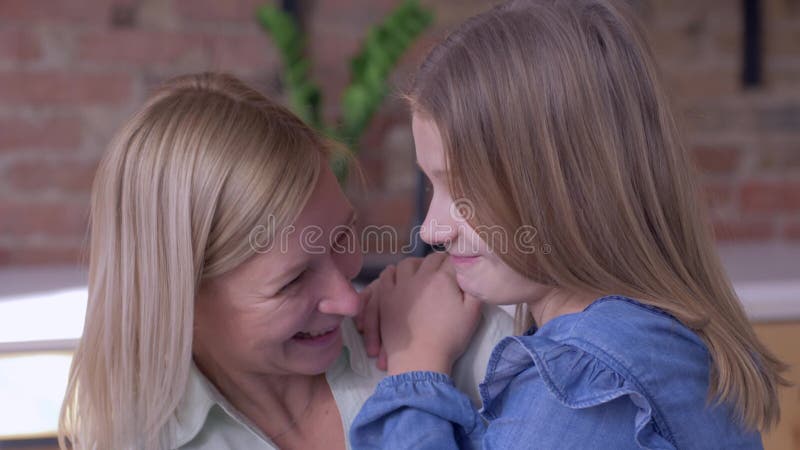 Happy motherhood, little smiling child girl tells beloved mum whispering secrets in ear at home