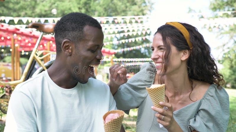 Happy multiracial couple have fun with ice cream in park