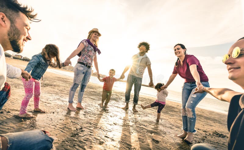 Happy multiracial families round dancing at the beach at sunset