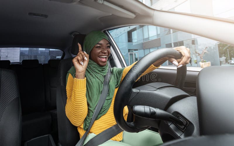 Happy muslim black female driver singing and dancing while driving car