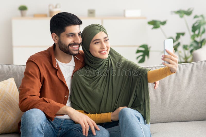 Happy Muslim Husband and Wife Making Selfie on Smartphone Indoor St