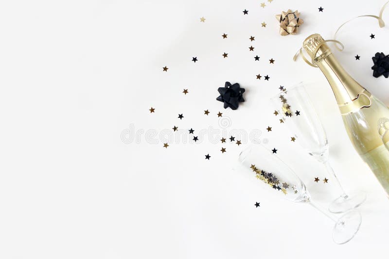 Happy New Year composition. Champagne wine bottle and glasses with golden confetti stars isolated on white table stock photo Happy New Year composition. Champagne wine bottle and glasses with golden confetti stars isolated on white table stock photo