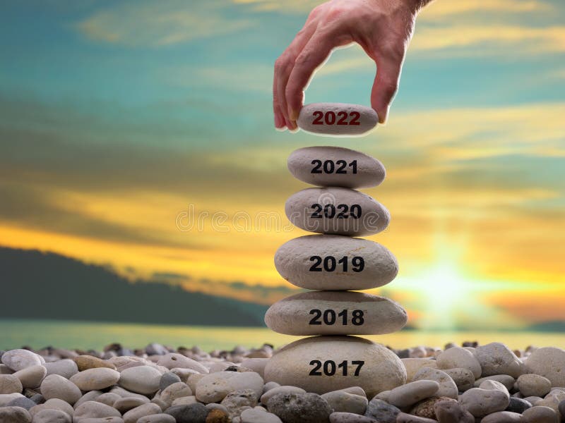 Happy new year 2022 concept. Years written on the rising stone pile. Man hand adding stone to tower. Background is blurred sunset sky stock images