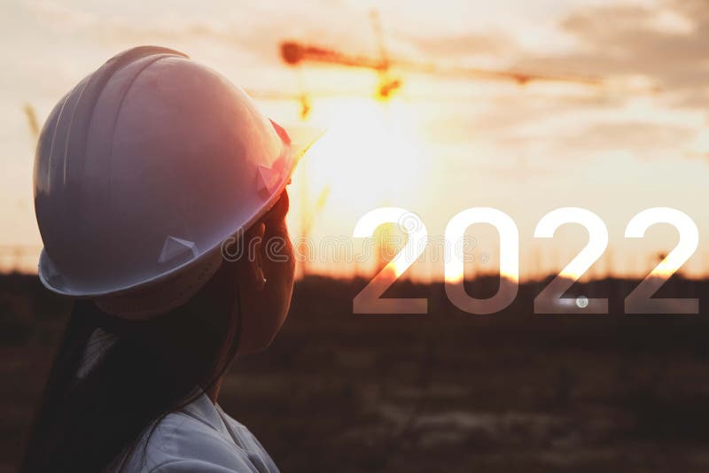 Happy New Year 2022 and Female construction engineer against the backdrop of construction site with cranes at sunset. woman