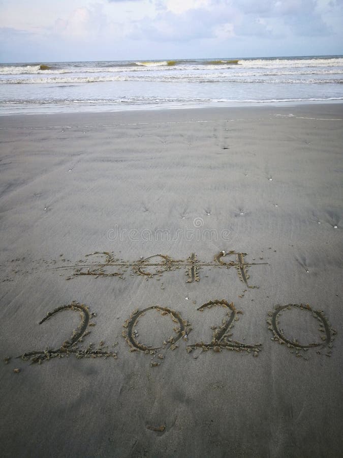 Happy new year 2020, lettering on the beach with wave and clear blue sea. Numbers 2020 year on the sea shore. royalty free stock photo