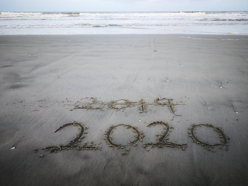 Happy new year 2020, lettering on the beach with wave and clear blue sea. Numbers 2020 year on the sea shore. royalty free stock photo