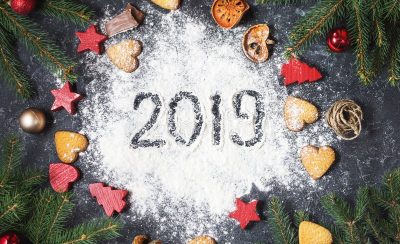 Happy New Year 2019 written on flour and Christmas Decorations Gingerbread cookies on dark stone background. New Year greeting car stock photo Happy New Year 2019 written on flour and Christmas Decorations Gingerbread cookies on dark stone background. New Year greeting car stock photo