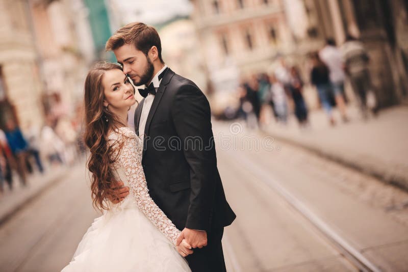 Happy newlyweds couple on a walk in old European town street, gorgeous bride in white wedding dress together with handsome groom