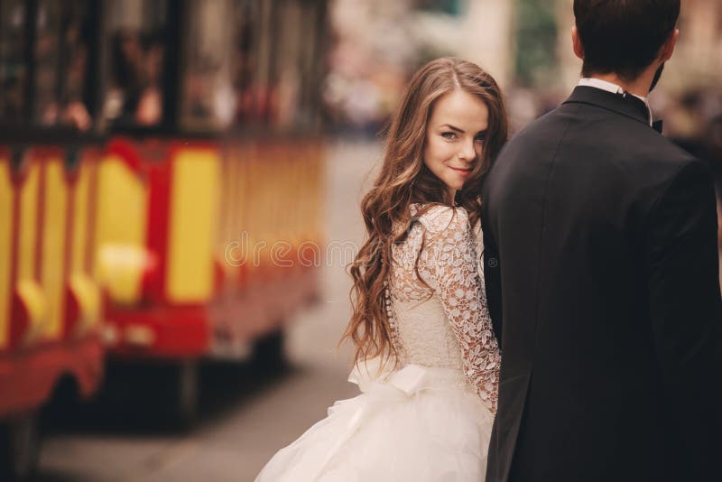 Happy newlyweds couple on a walk in old European town street, gorgeous bride in white wedding dress together with handsome groom