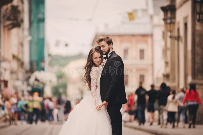 Happy newlyweds couple on a walk in old European town street, gorgeous bride in white wedding dress together with handsome groom