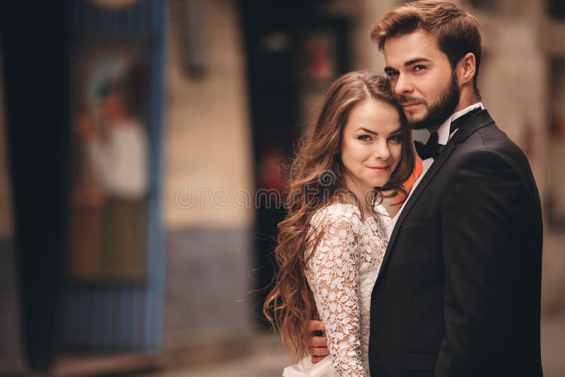 Happy newlyweds couple on a walk in old European town street, gorgeous bride in white wedding dress together with handsome groom