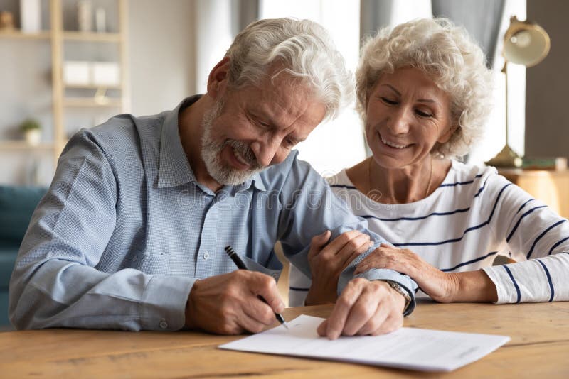 Happy old mature retired family couple putting signature on paper document.