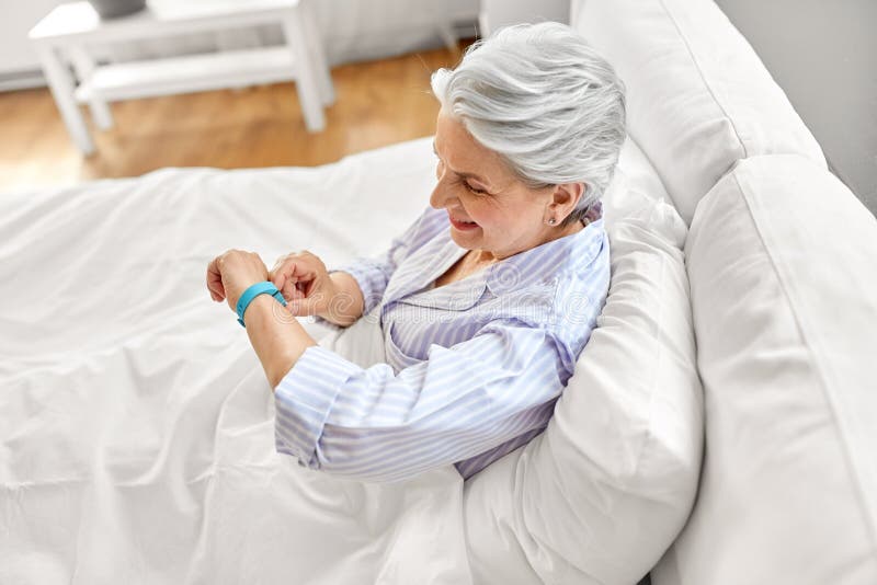 happy old woman with health tracker sitting in bed