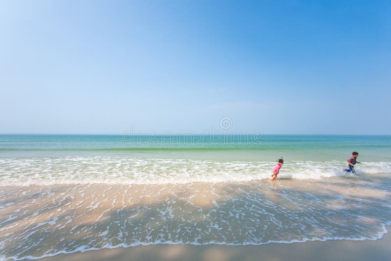 Happy older brother and little sister playing and surfing on white sand beach, light blue sky backgrounds. Summer season. Sunny stock photography Happy older brother and little sister playing and surfing on white sand beach, light blue sky backgrounds. Summer season. Sunny stock photography