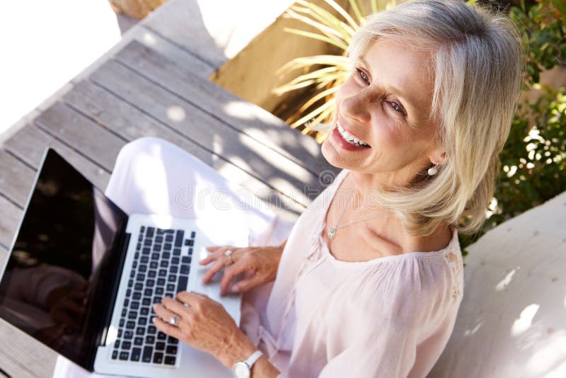 Happy older woman with laptop computer sitting outside royalty free stock photography