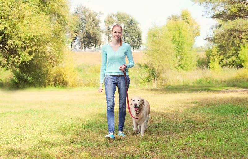 Felice possessore donna e Golden Retriever cane camminare insieme nel parco estivo.