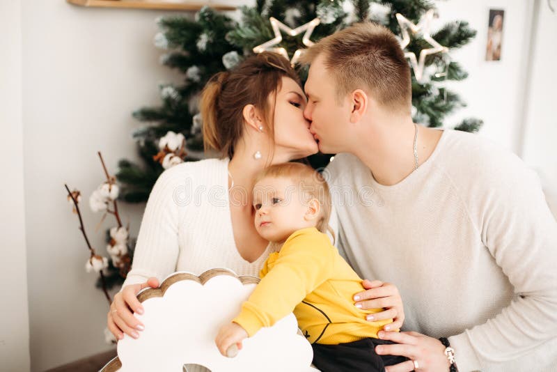 Happy parents in love hugging and kissing sitting on background near Christmas tree. royalty free stock images Happy parents in love hugging and kissing sitting on background near Christmas tree. royalty free stock images