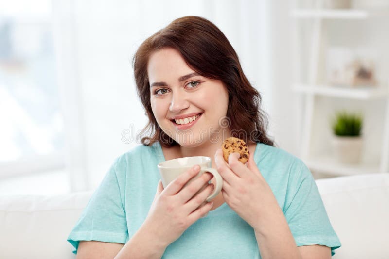 Happy plus size woman with cup and cookie at home