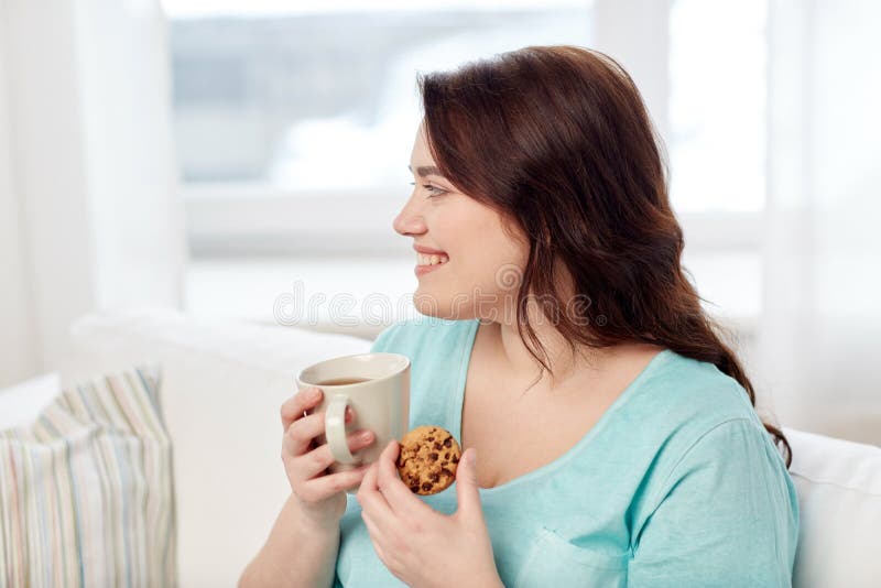 Happy plus size woman with cup and cookie at home