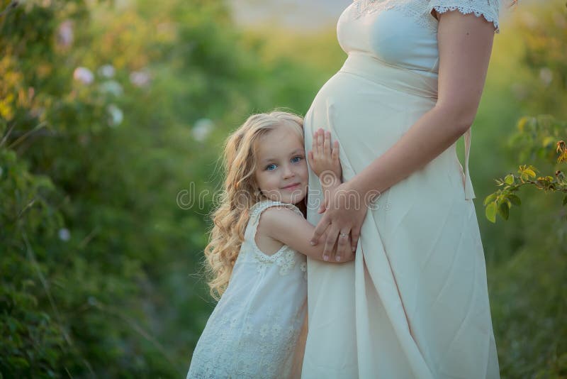 Happy pregnant woman with little daughter in a green tea rose garden