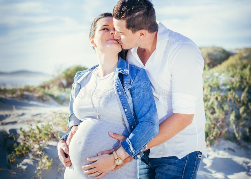 Happy pregnant young couple interacting, standing outdoors kissing, beach scene stock photography Happy pregnant young couple interacting, standing outdoors kissing, beach scene stock photography