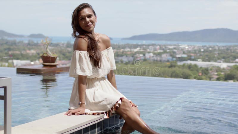 Happy relaxed woman sitting poolside against ocean coast