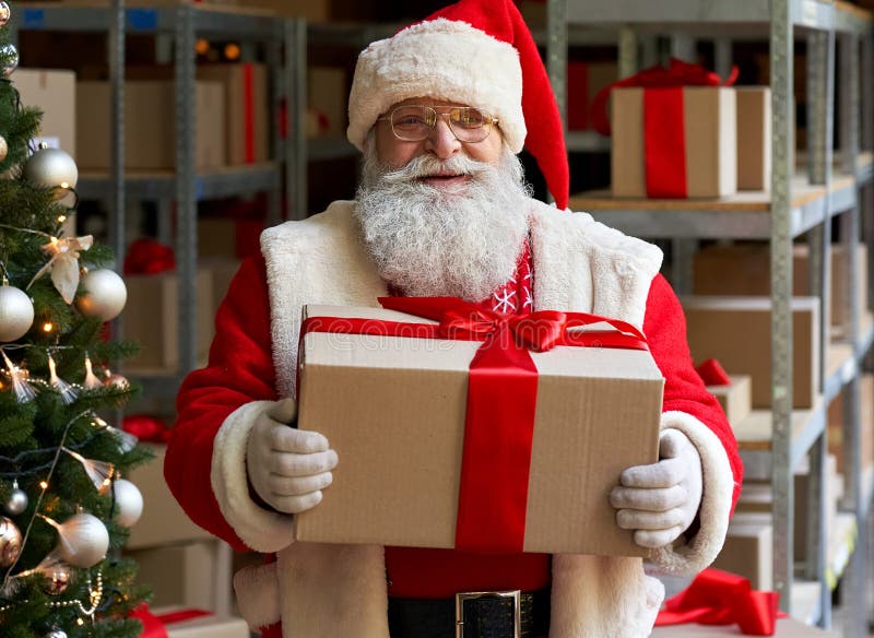 Happy Santa Claus wearing costume holding gift box in workshop, portrait.