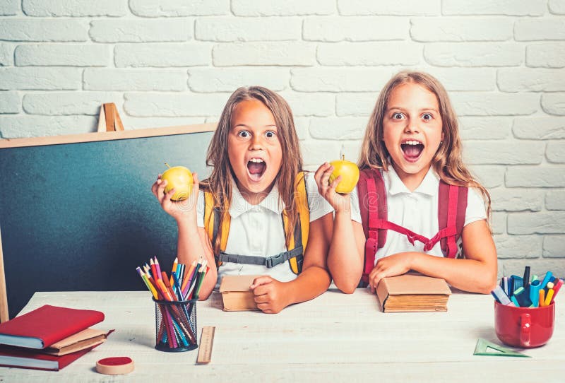 Happy school kids at lesson in september 1. Little girls eat apple at lunch break. School time of girls. Friendship of