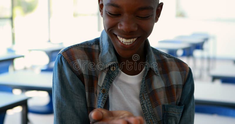 Happy schoolboy looking at hand in classroom