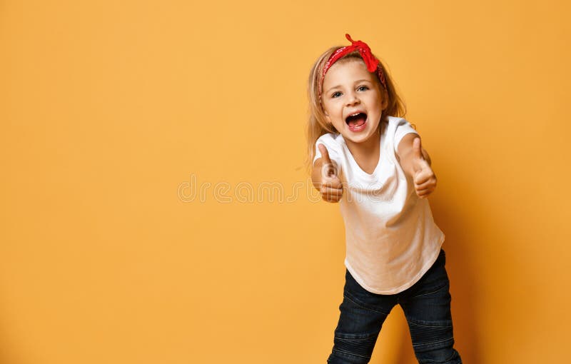 Happy screaming kid girl in a white t-shirt and a red bandage on her head is showing thumbs up on yellow with copy space