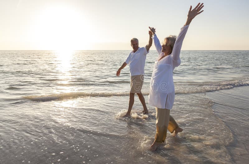 Felice senior, uomini e donne, coppia di danza e si tengono per mano in una deserta spiaggia tropicale all'alba o al tramonto.