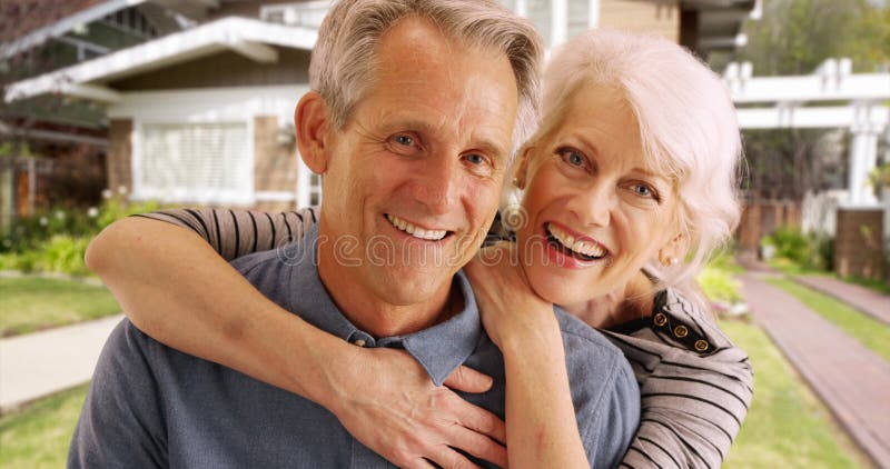 Happy senior couple laughing and smiling in front of their house.