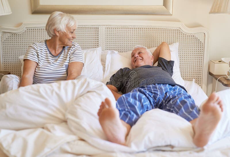 Content senior couple smiling at each other while relaxing in bed together in the morning. Content senior couple smiling at each other while relaxing in bed together in the morning