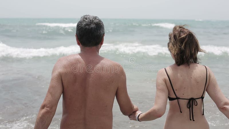 Happy senior couple walking together into the sea