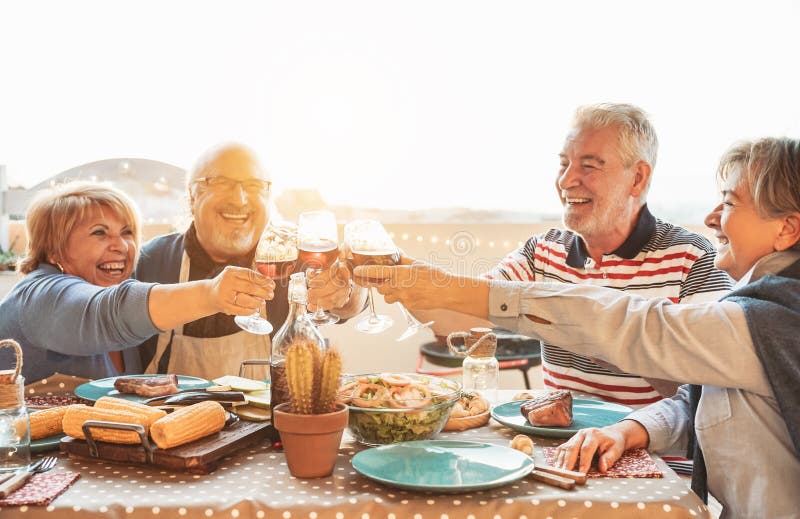 Happy senior dining and tasting red wine glasses in barbecue dinner party - Family having fun enjoying bbq at sunset time