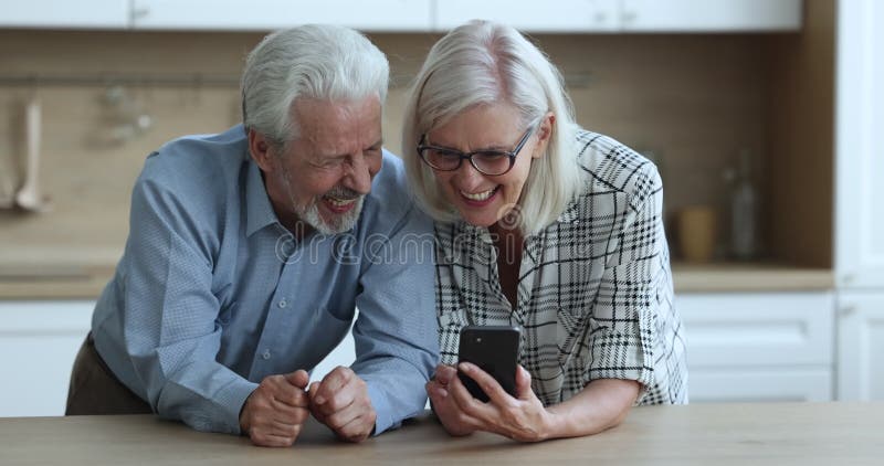 Happy senior married couple using smartphone at home together