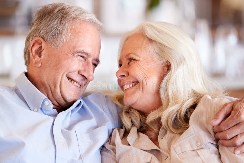 Happy senior white couple sit at home embracing, smiling at each other, head and shoulders, close up