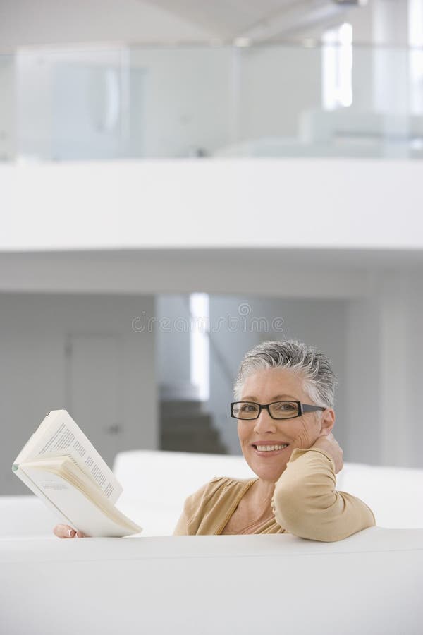 Happy Senior Woman Reading Book On Sofa