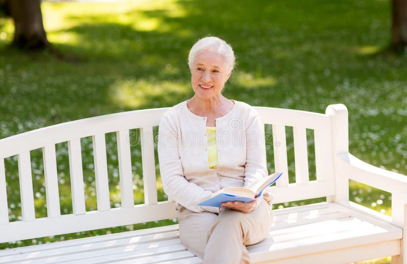 Old age, retirement and people concept - happy senior woman reading book sitting on bench at summer park. Old age, retirement and people concept - happy senior woman reading book sitting on bench at summer park