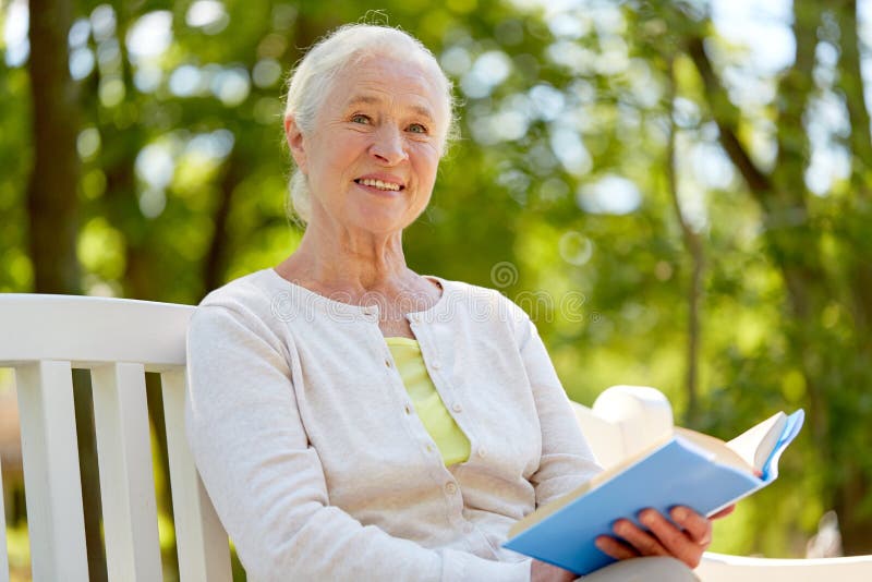 Old age, retirement and people concept - happy senior woman reading book sitting on bench at summer park. Old age, retirement and people concept - happy senior woman reading book sitting on bench at summer park