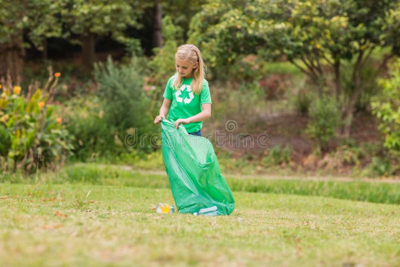 School-age girl holding green trash bag and picking up plastic bottles and litter at park stock photography