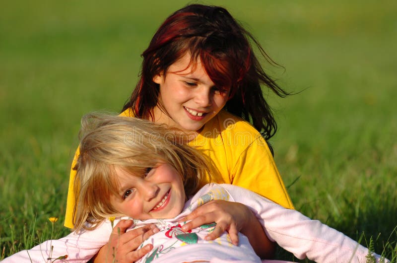 Dve kaukazských biele sestry s blondínka a brunetka chĺpky, hrá v zelenej tráve, baví spolu a byť šťastnými v slnečný deň.