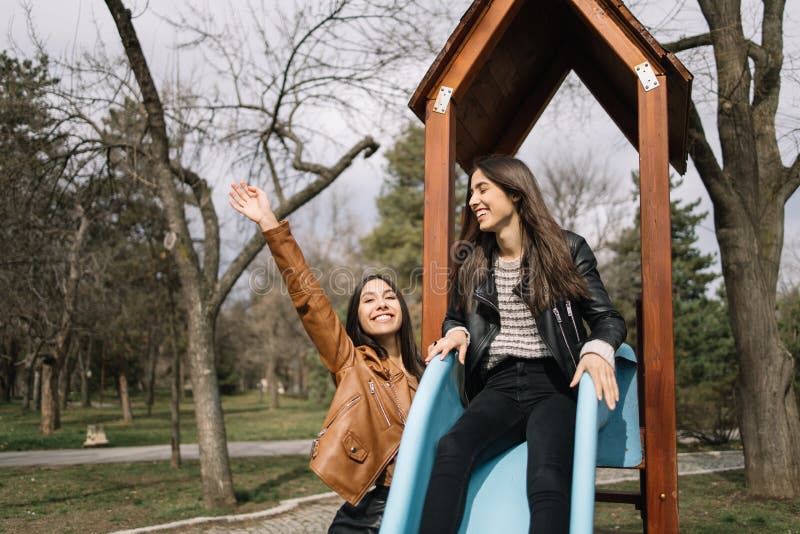 Happy sisters having fun on a slide together. Pretty young girls enjoying a slide in play park in spring day.