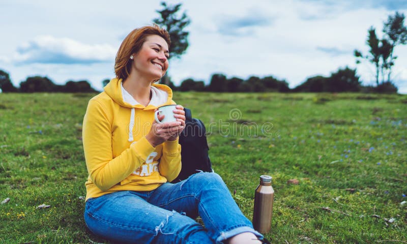 Happy smile girl holding in hands cup of hot tea on green grass in outdoors nature park, beautiful young woman hipster enjoy drink stock image Happy smile girl holding in hands cup of hot tea on green grass in outdoors nature park, beautiful young woman hipster enjoy drink stock image