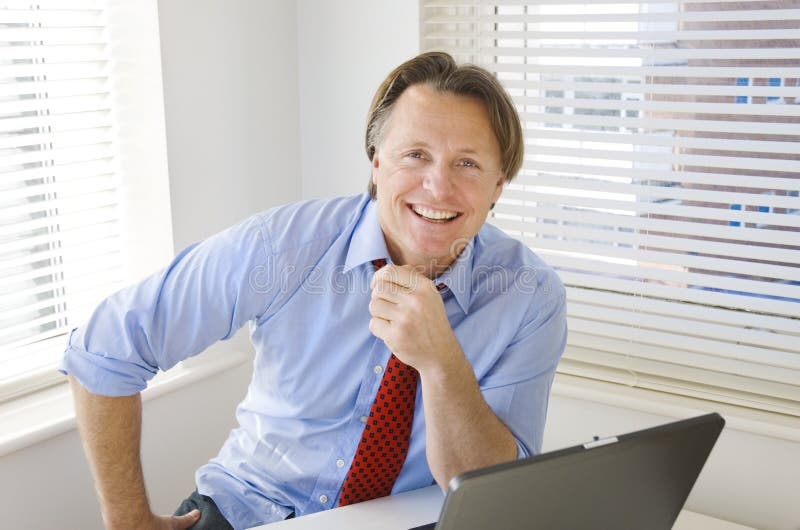 Un bel quarantenne imprenditore è sorridente come si siede davanti al suo computer portatile nel suo ufficio.